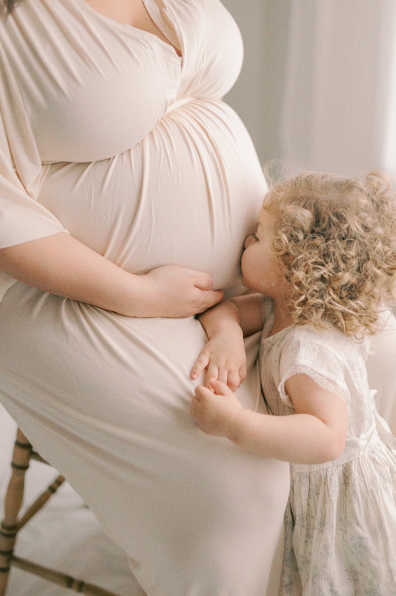 A pregnant mother sits on a stool while her toddler daughter kisses her bump Prenatal Classes Seattle