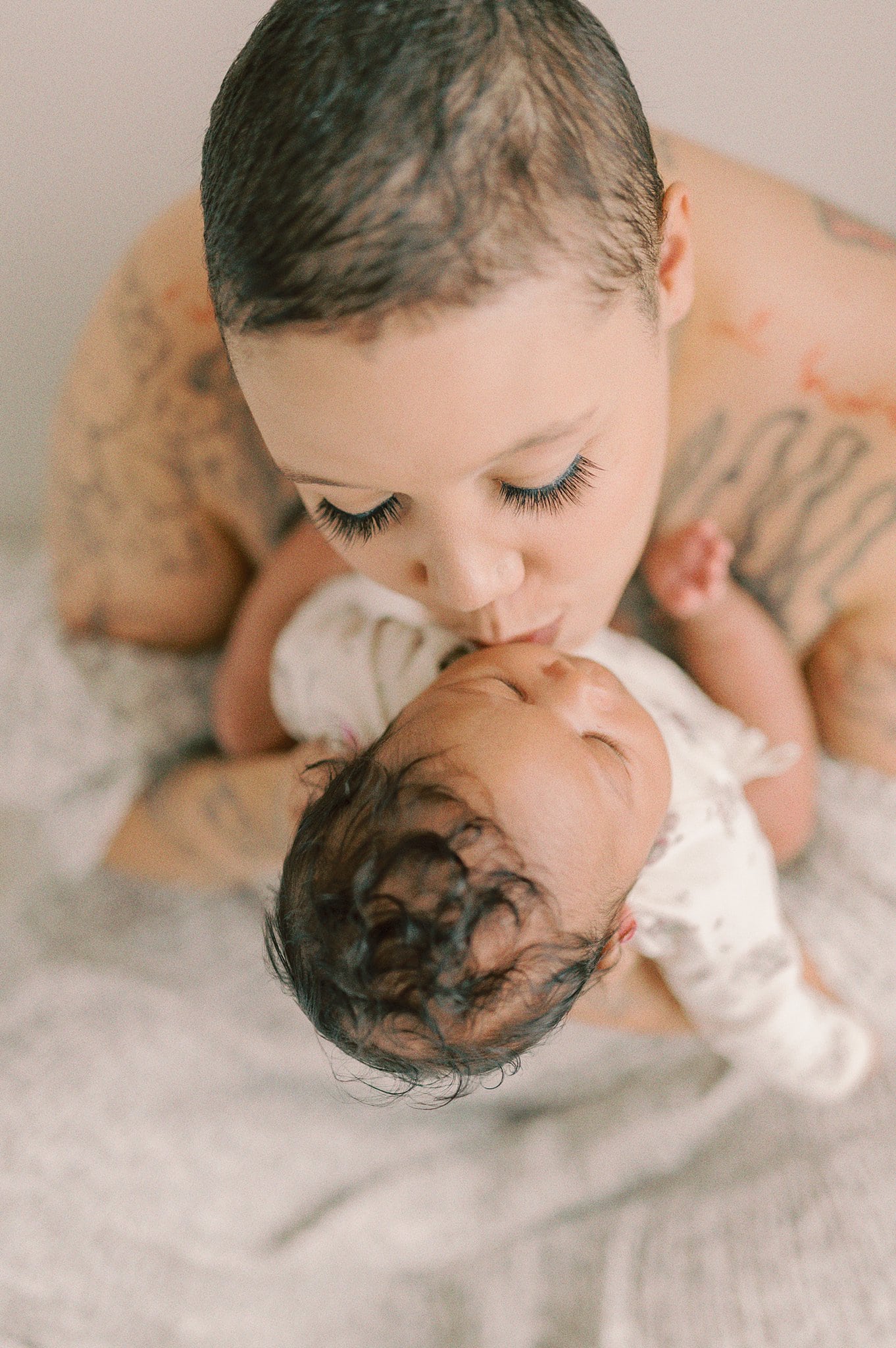 A new mother kisses the cheek of her newborn baby while sitting in a studio