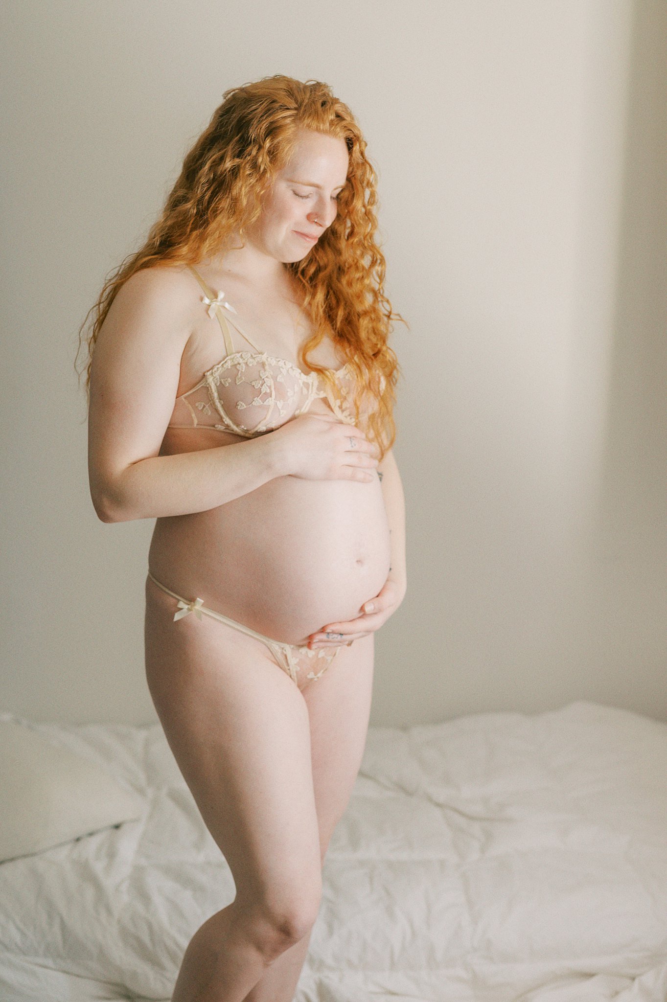 A pregnant woman looks down at her bump while standing in lace lingerie Seattle Botox