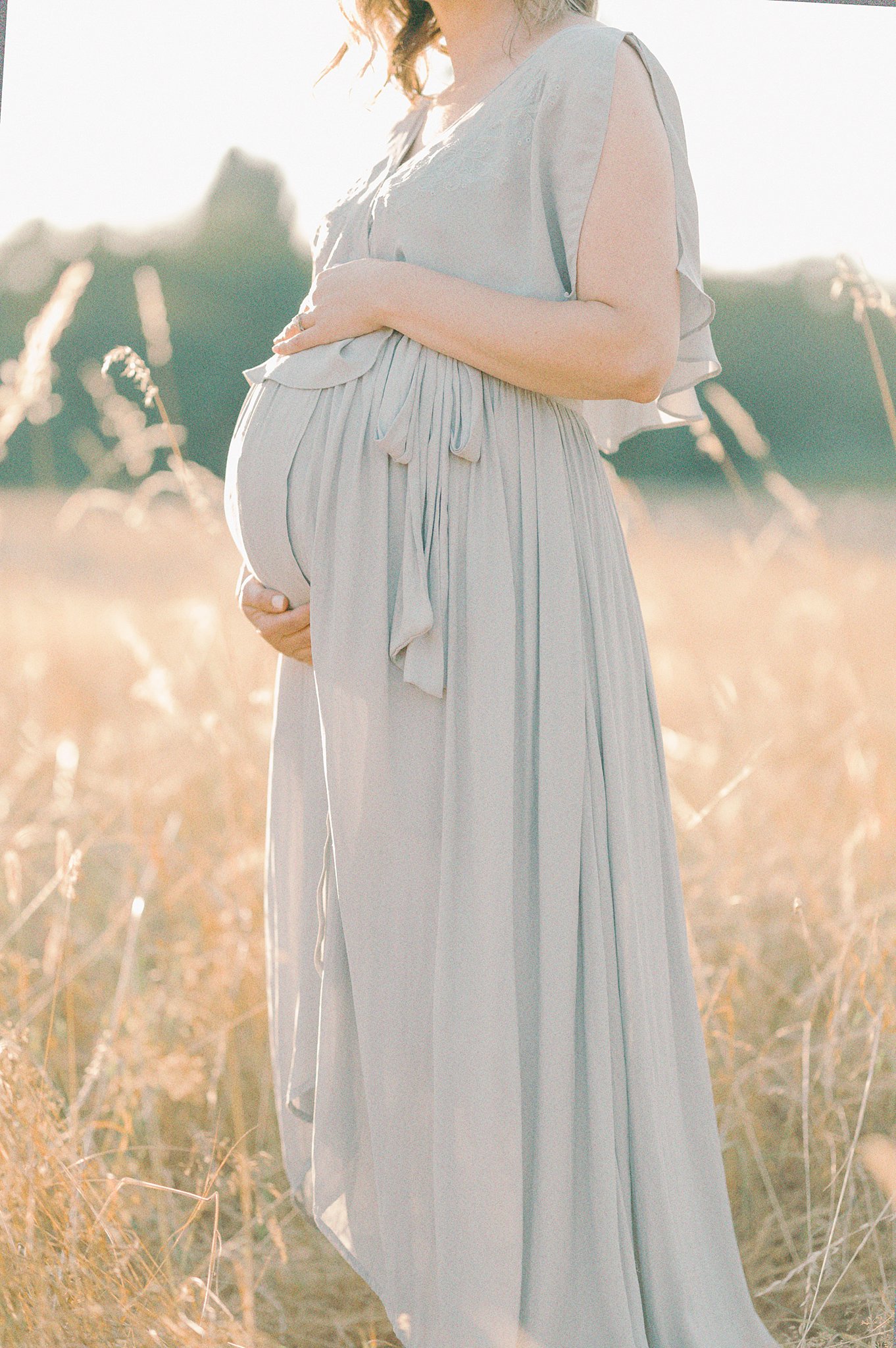 Details of a mother to be standing in a golden field of grass holding her bump