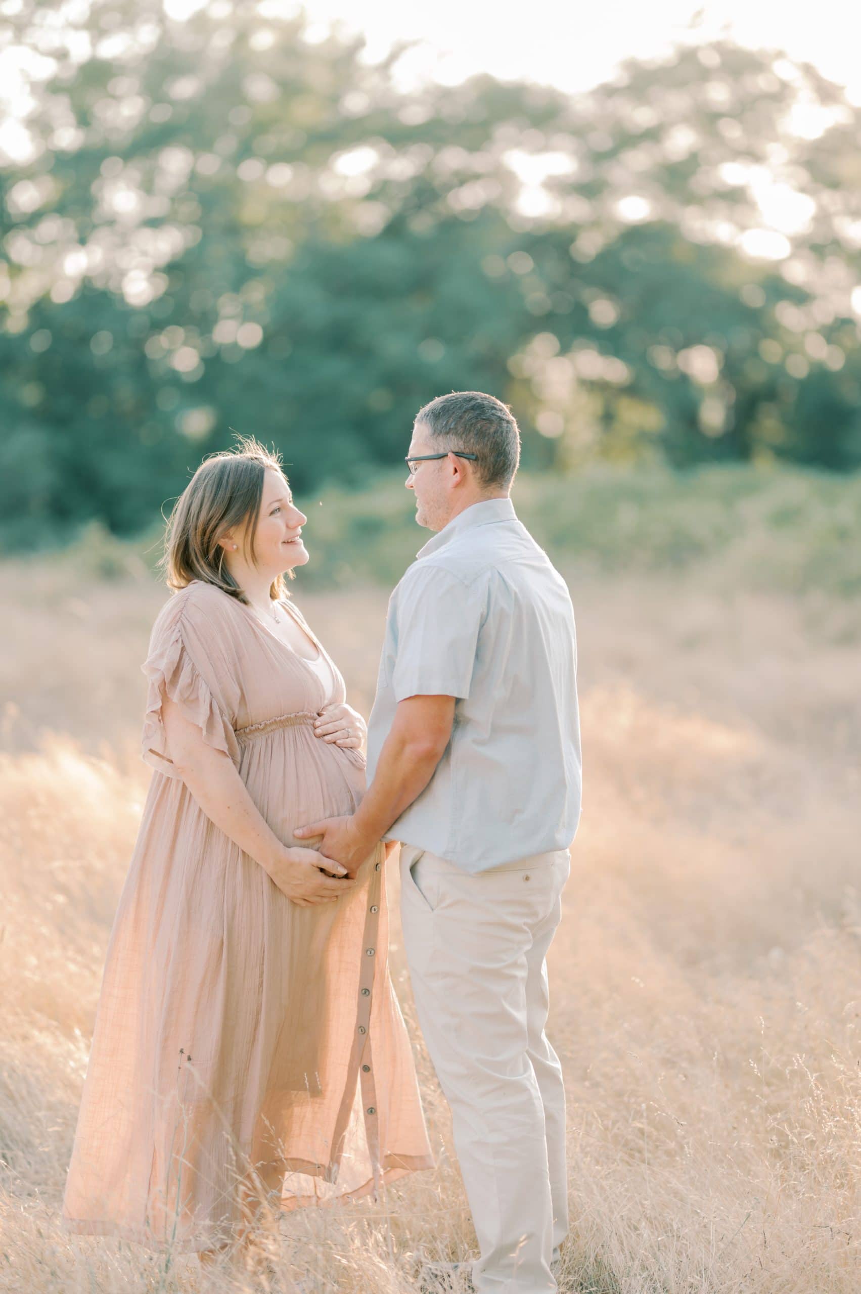 A mom to be holds the hand of her partner on her bump while standing in a field of tall grass
