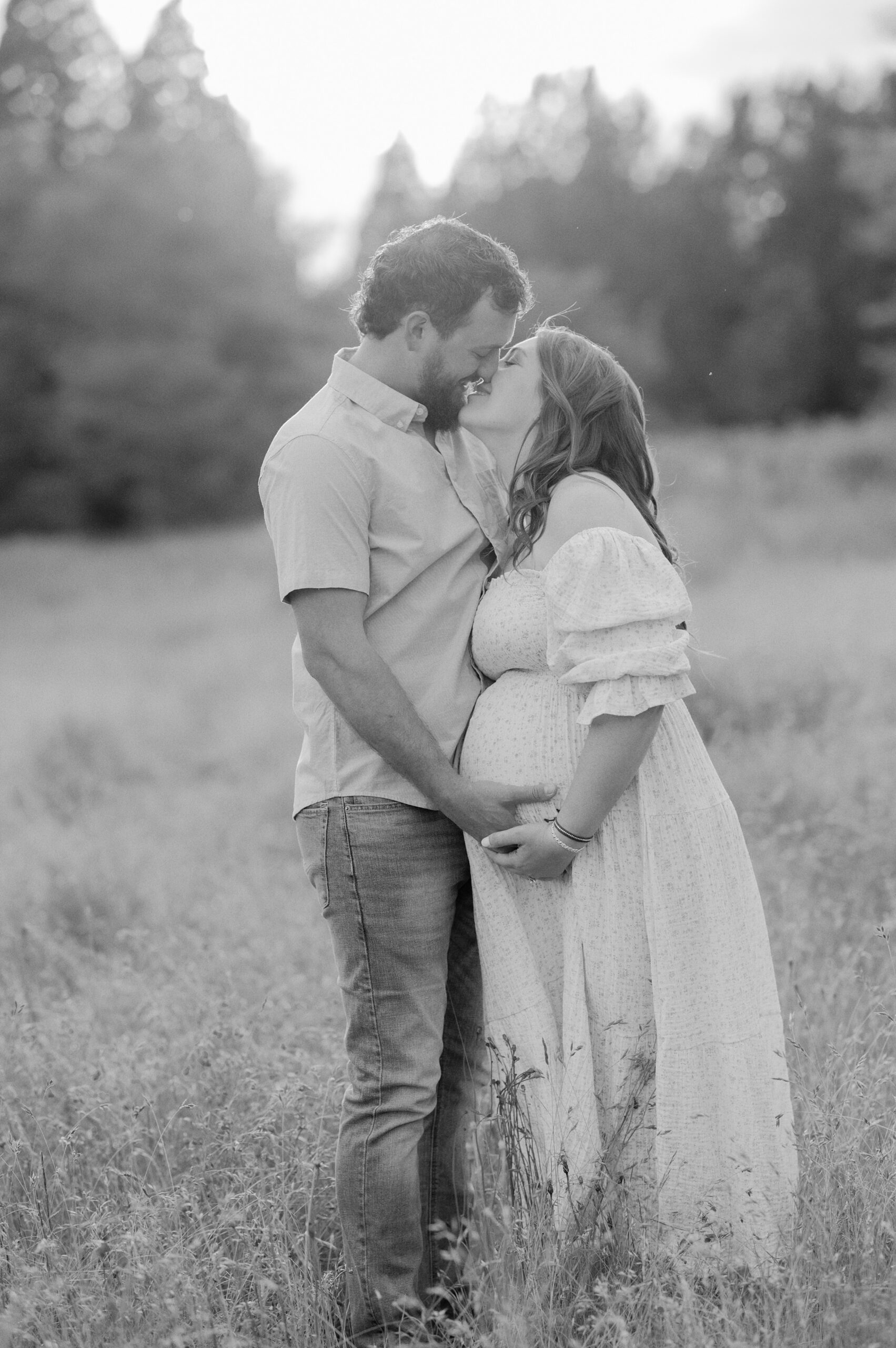Parents to be kiss while holding the bump in a large open field of tall grass