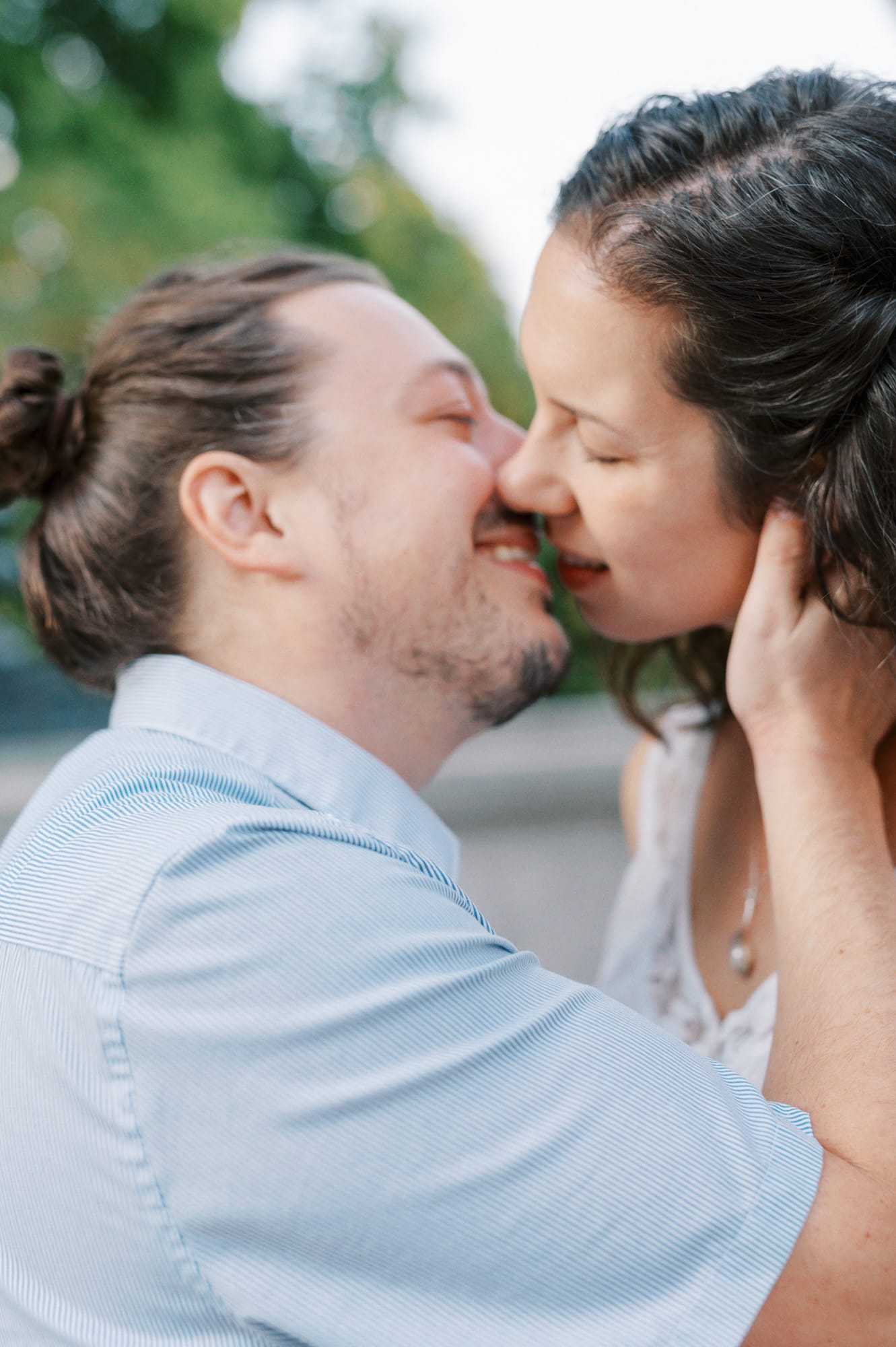 A couple in blue kisses while standing in a park at sunset