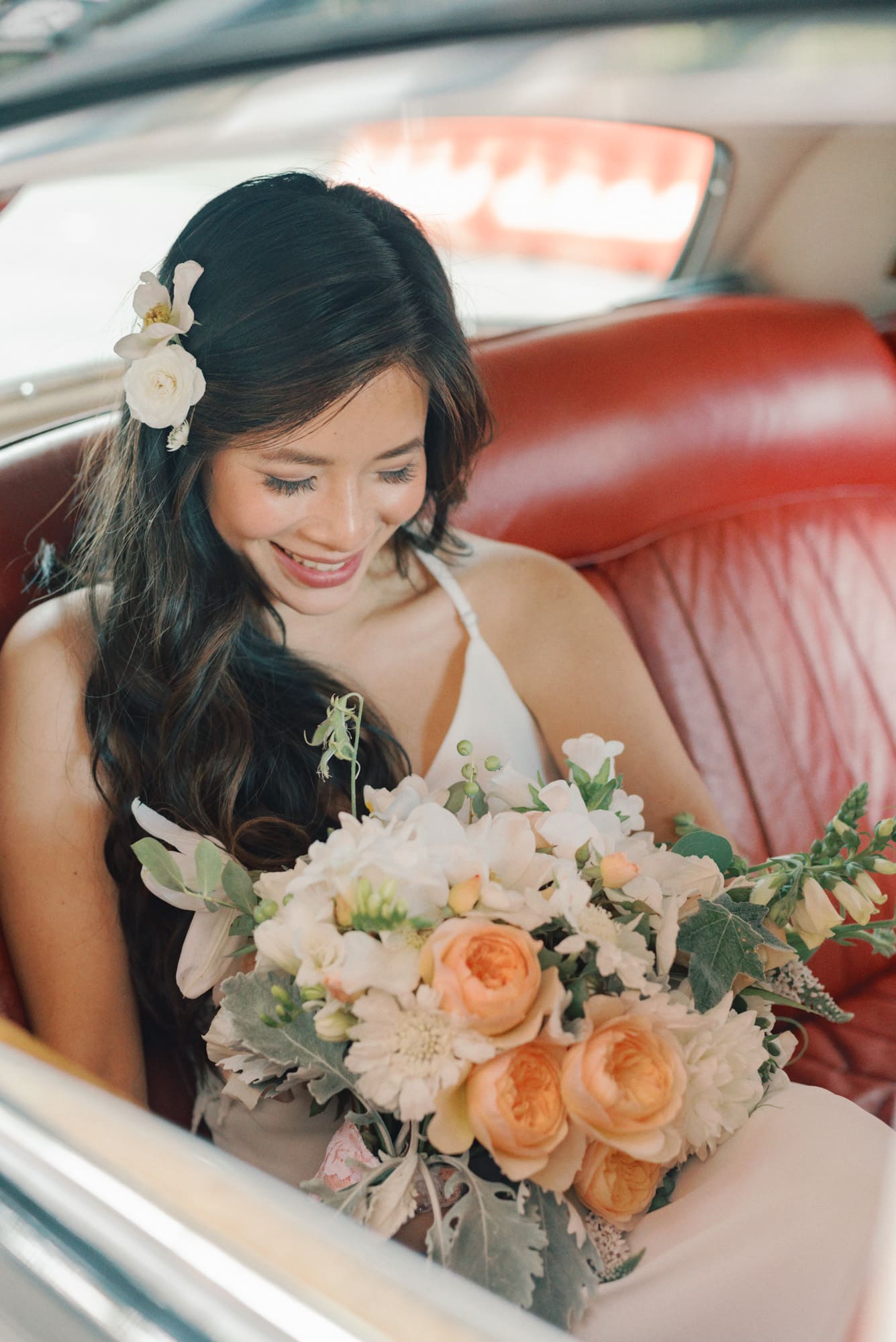 A bride smiles down at her bouquet while sitting in a vintage car at her Chihuly Garden and Glass wedding