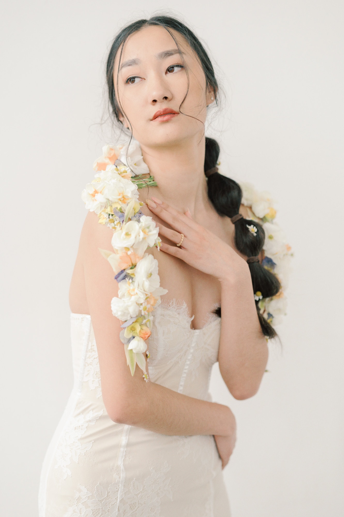 A bride in a lace dress stands with a hand on her chest and flowers on her shoulders before her Sodo Park Wedding