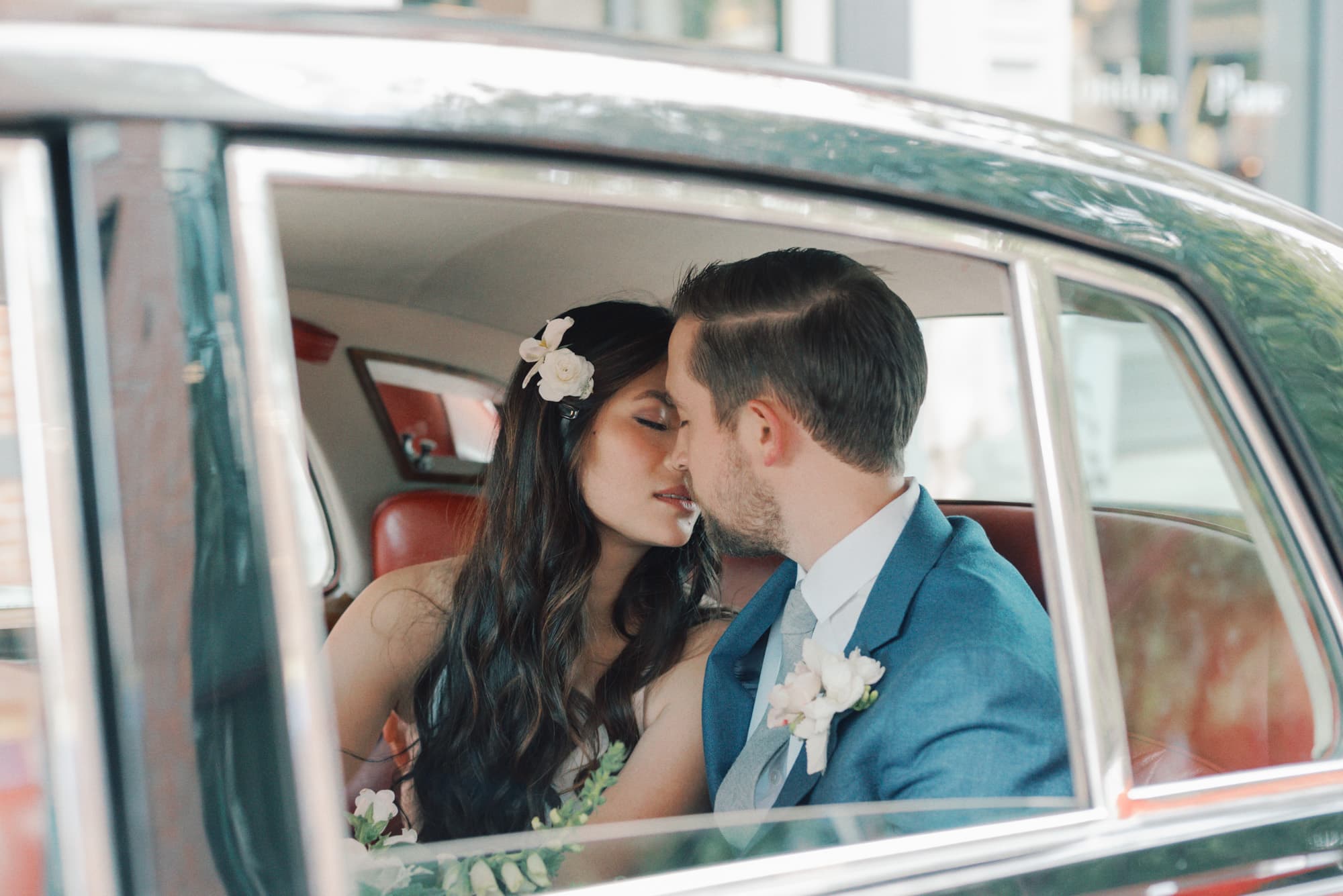 Newlyweds lean in for a kiss while sitting in the back of an antique car with red leather at their WithinSodo Wedding